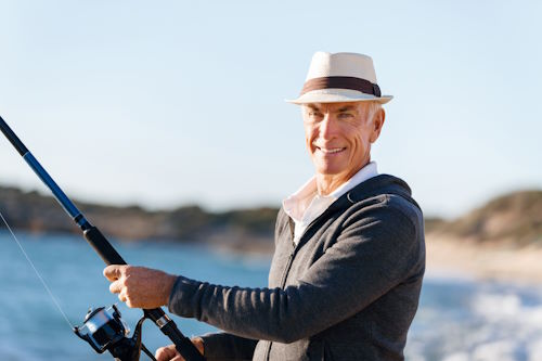 A man wearing a hat fishing by a lake